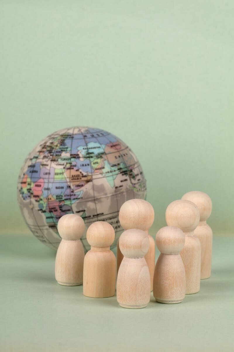 Wooden figures grouped around a globe on a soft green backdrop, symbolizing global unity.