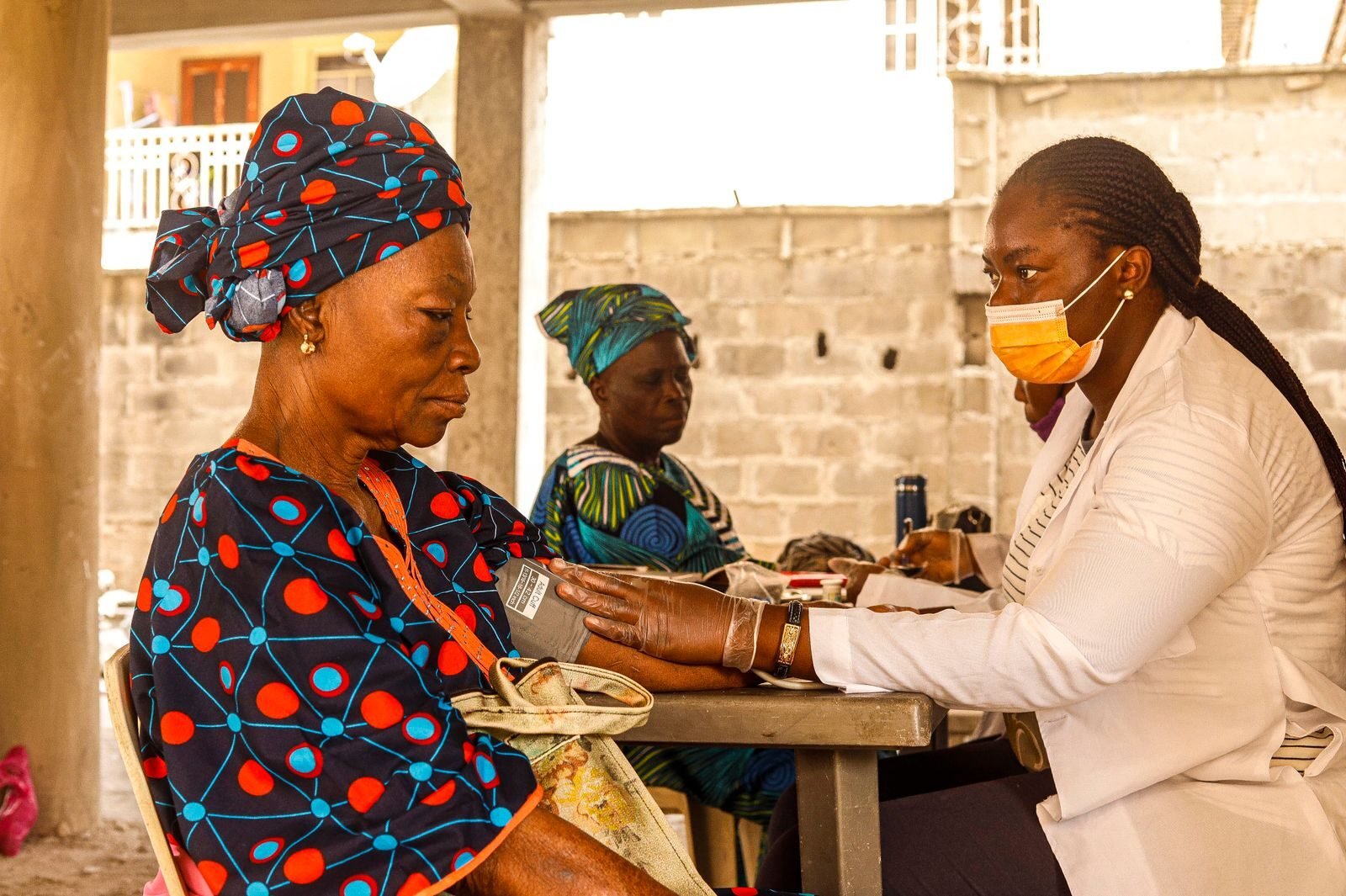The Complete Guide to Becoming a Professional Nurse in The Gambia A healthcare worker checks blood pressure of an elderly woman in a rural clinic setting.